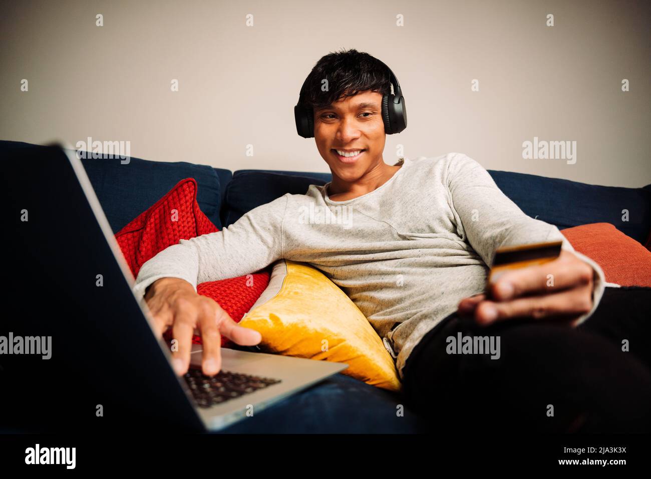 Asian man working on laptop making credit card payment and listening music Stock Photo