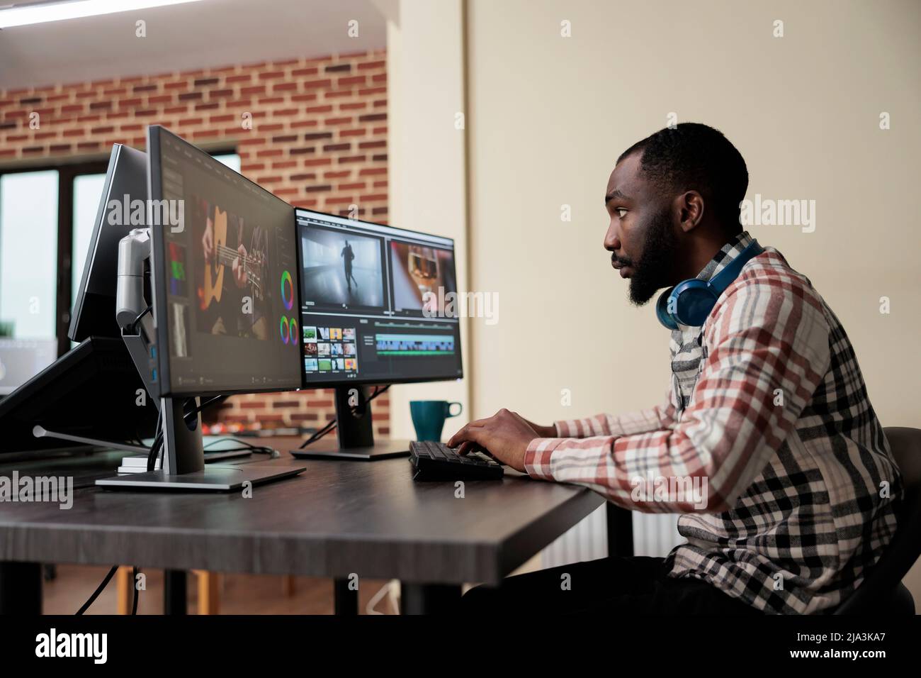 Video production house employee sitting at multi monitor workstation
