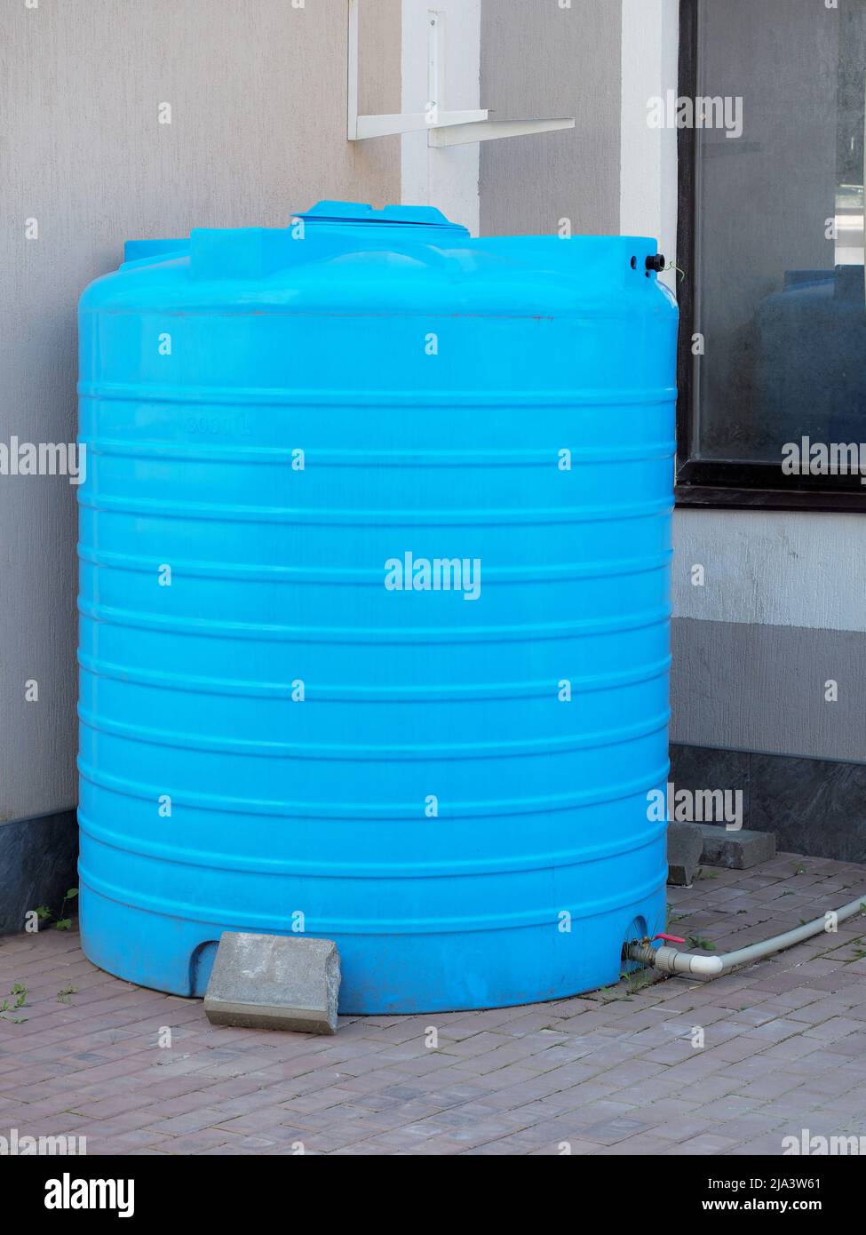 A blue cylindrical water tank with hose connected to it stands against