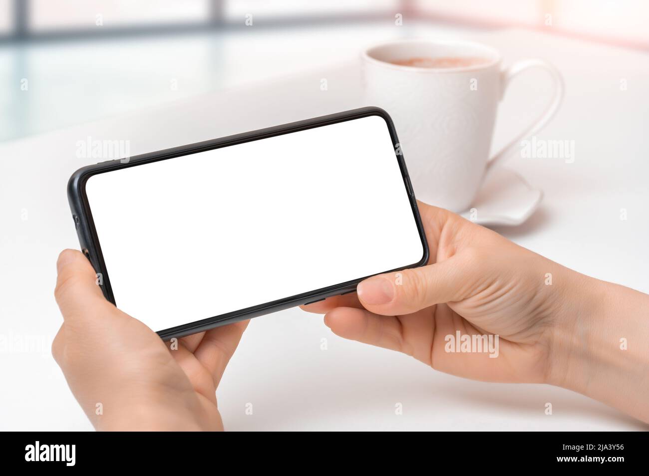 mockup cellphone horizontal position. Mockup image of woman holding black mobile phone with blank screen with coffee cup on table. Closeup of woman ha Stock Photo