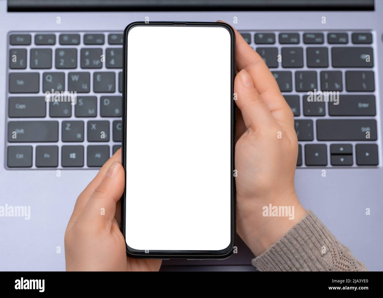hands of woman with cell phone with blank screen on laptop keyboard background. Top view mockup image of hands holding blank white screen mobile phone Stock Photo