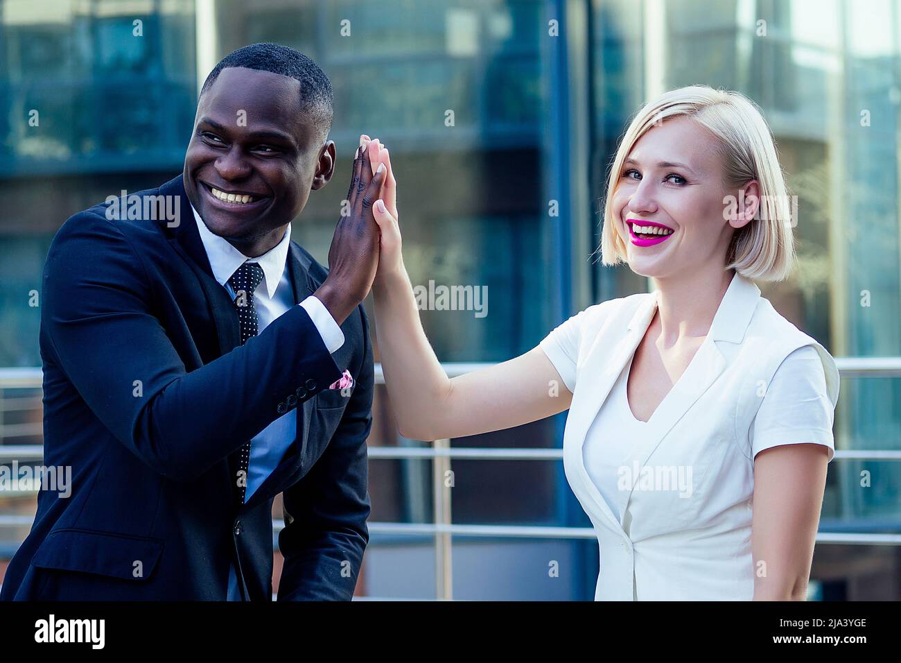 handsome African American businessman in a stylish black suit talking high five with attractive blonde woman business lady on the street background Stock Photo