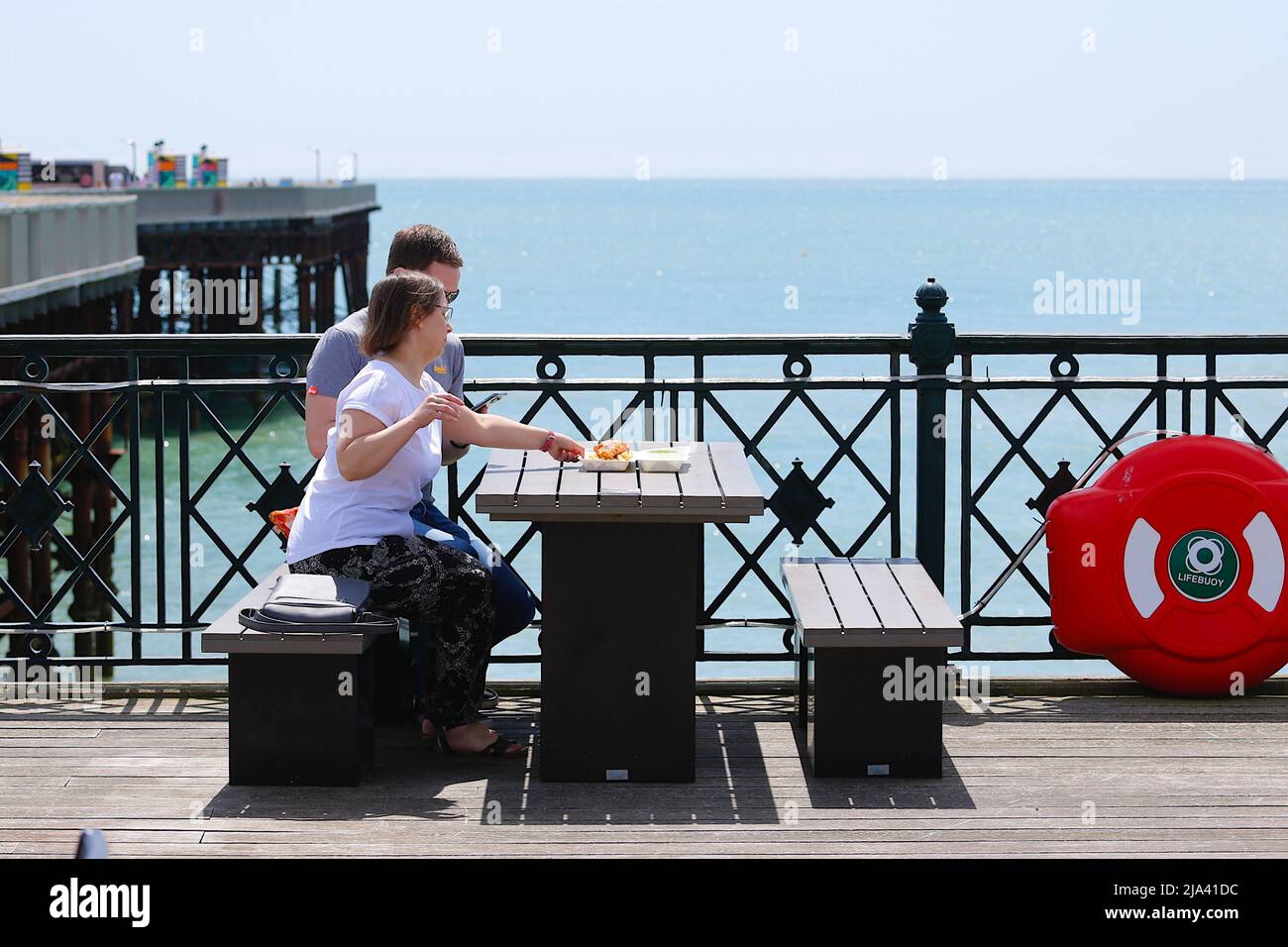 Hastings, East Sussex, UK. 27 May, 2022. UK Weather: Sunny intervals in the seaside town of Hastings in East Sussex as Brits enjoy the warm weather today along the seafront promenade. A couple eating fish and chips on the Hastings pier. Photo Credit: Paul Lawrenson /Alamy Live News Stock Photo