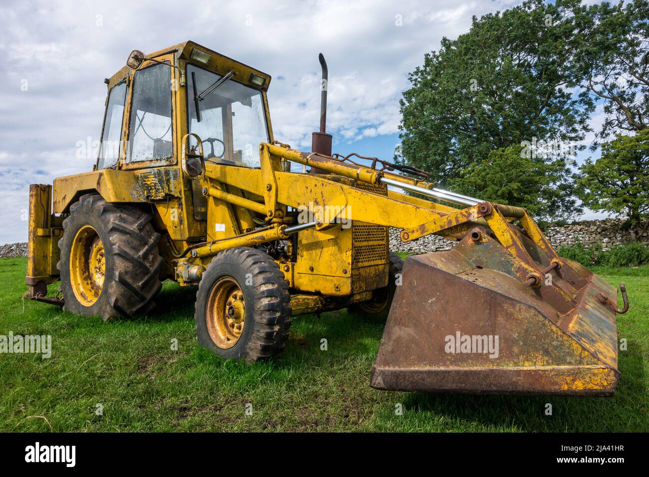 An old Ford backhoe loader rests in the sunshine of a field near Appleby, Yorkshire. Spotted while doing the Dales High Way walk. Stock Photo