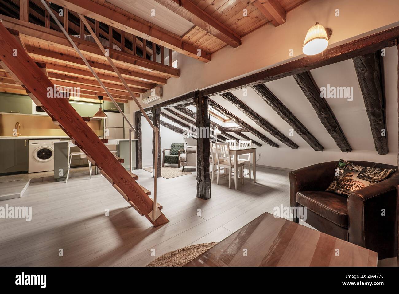 living room of a studio apartment with wooden beams and columns on the sloping ceilings, wooden staircase and open kitchen in the background Stock Photo