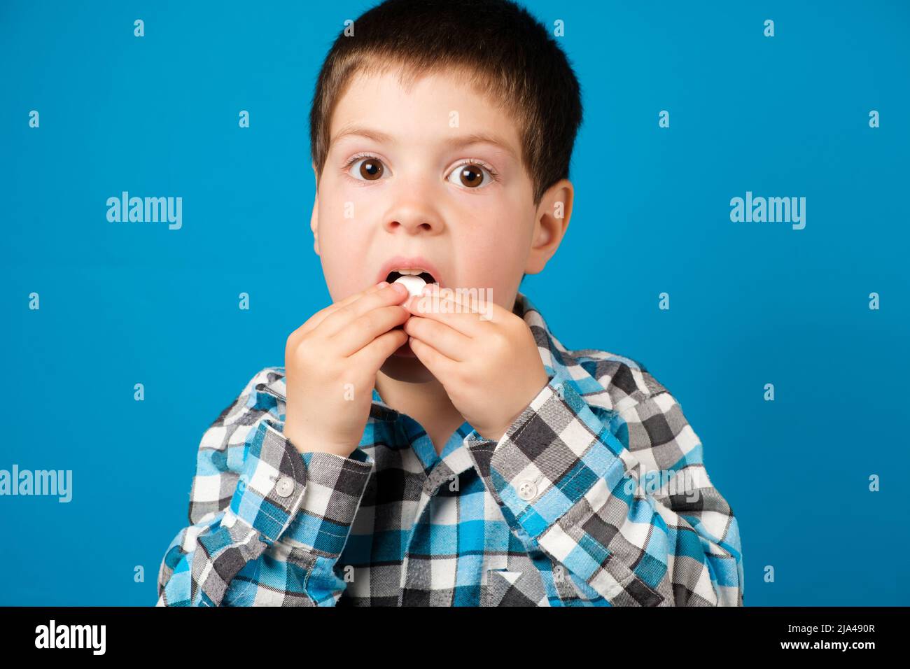 A beautiful preschool boy eats vitamin C or other medicine or dietary supplement on a blue background. Stock Photo