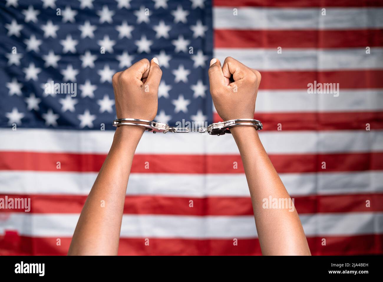 Close up shot of hanads rising with cuffs against us or american flag - concept of juneteenth, freedom and punishment. Stock Photo