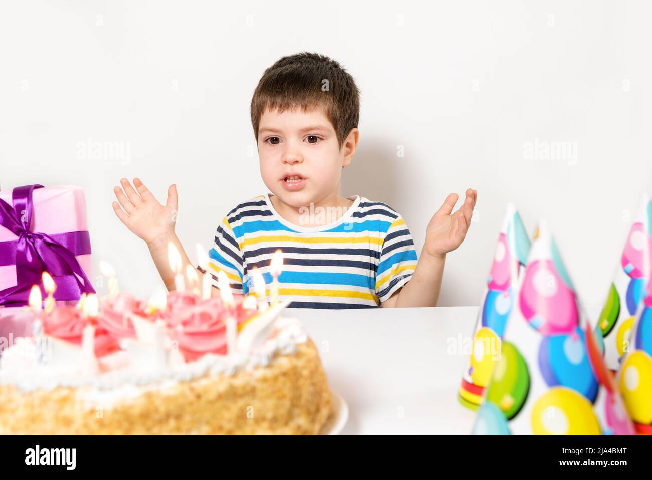 A handsome preschool boy with a cake on his birthday claps his hands on