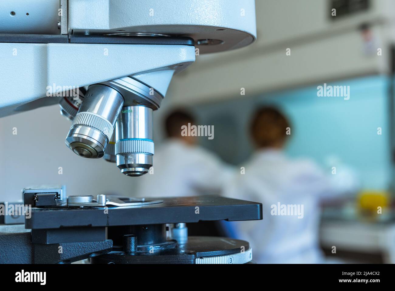 Close up of the lenses of a microscope with two scientists working on