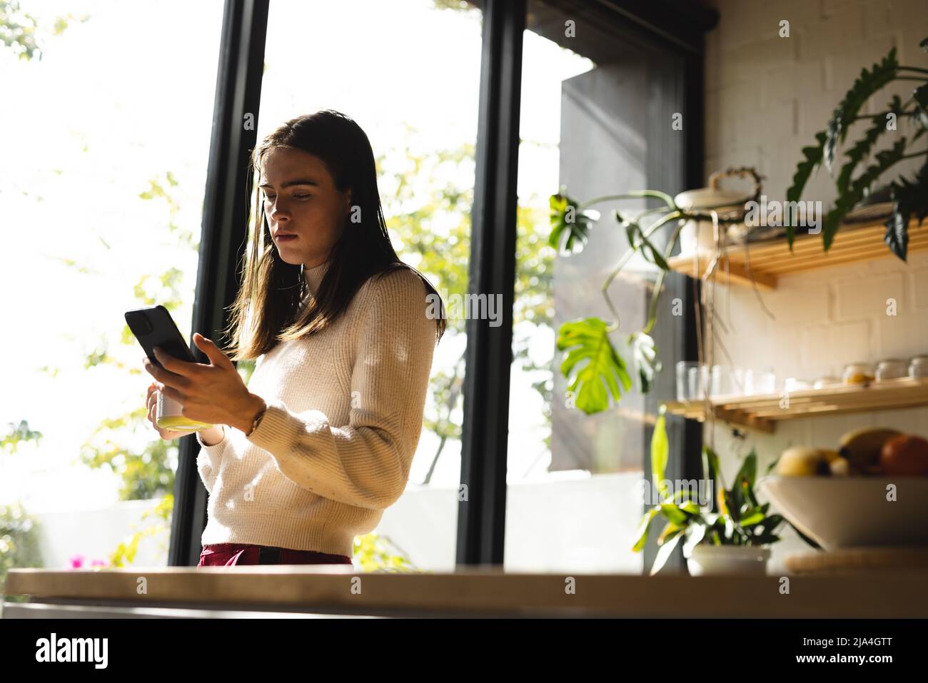 Thoughtful non-binary trans woman using smartphone near the window at home Stock Photo