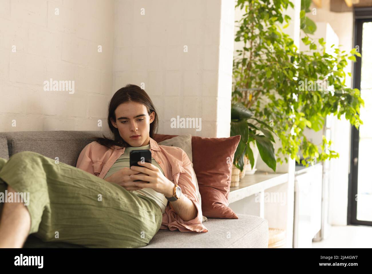 Nonbinary trans woman using smartphone lying on the couch at home