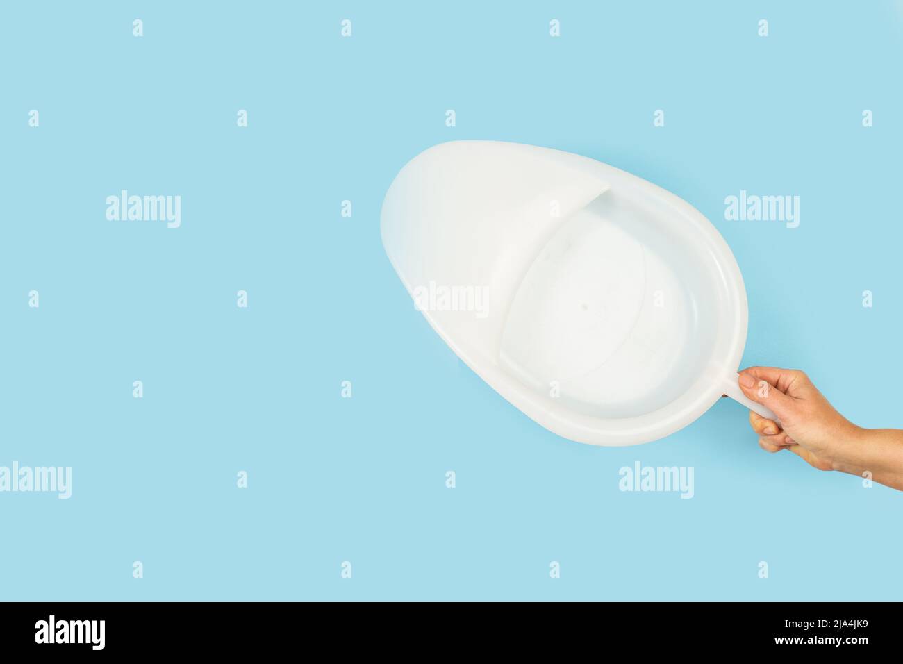 Woman hand holding a white plastic urinary bedpan on a light blue