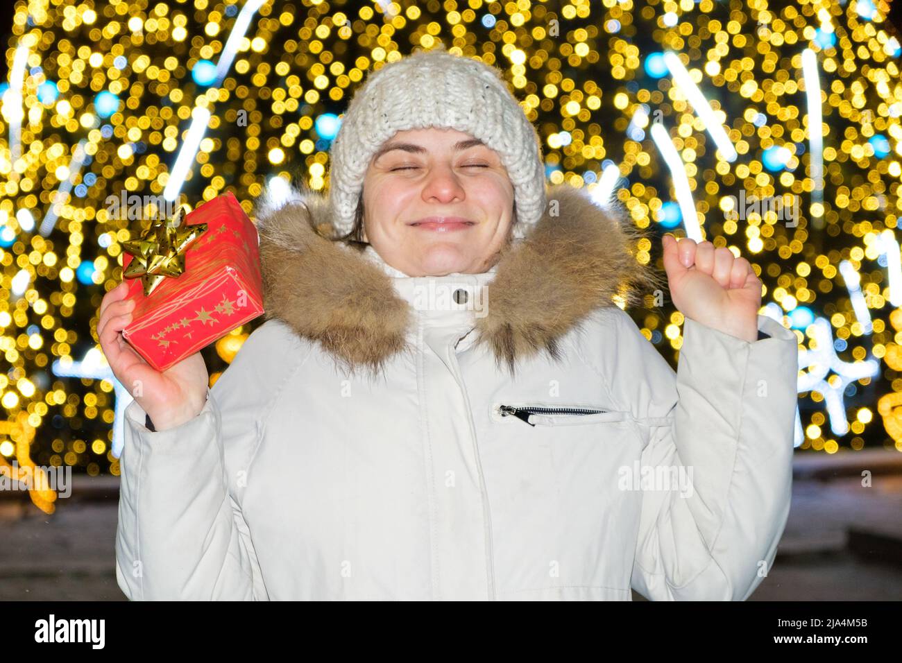 A happy young woman in front of a Christmas tree with bokeh holds a