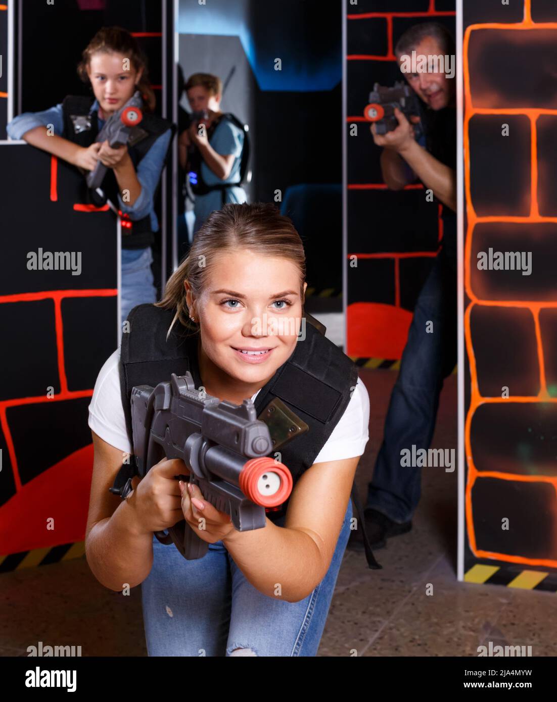 positive girl with laser pistol playing laser tag with friends Stock