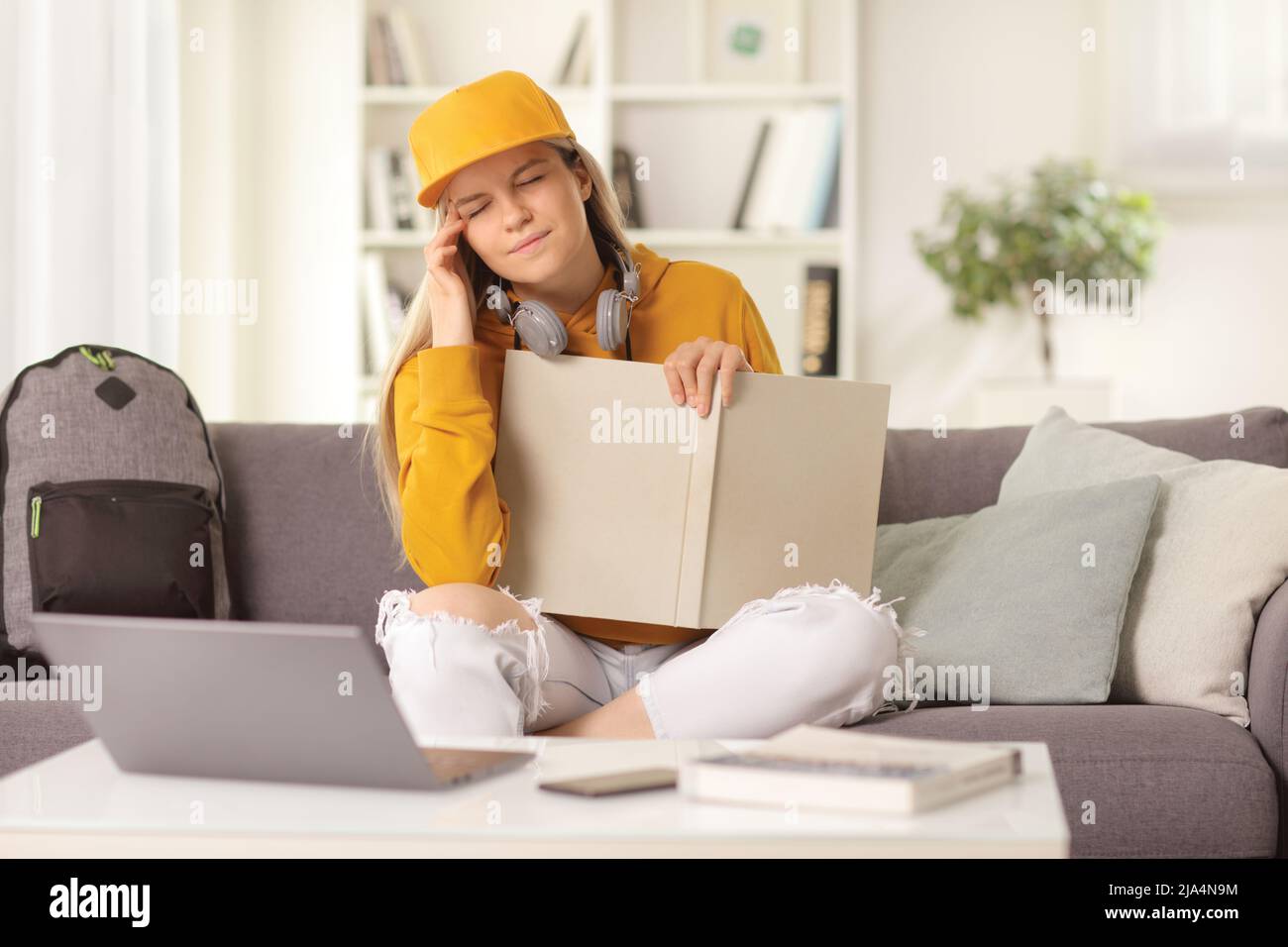 Young female studying on a sofa at home with a book trying to remember something Stock Photo