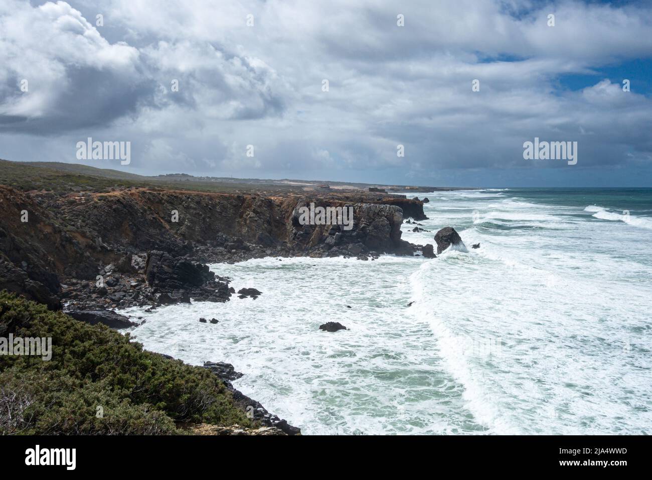 Large and numerous Atlantic Oceas waves rolling into the rocky coastline by Guincho Beach - Praia do Guincho with dramatic clouds in the sky against t Stock Photo