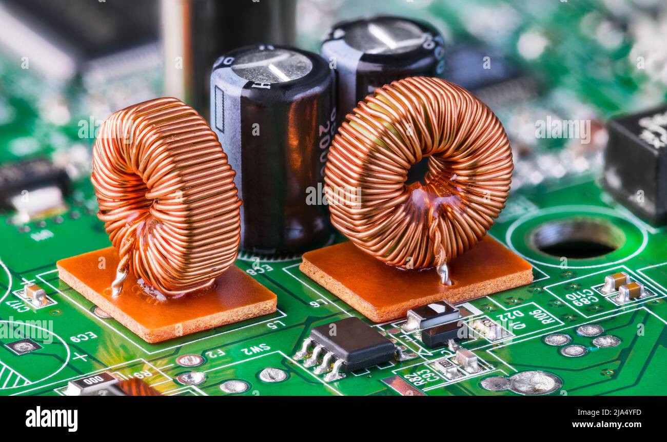 Closeup of toroidal inductors and electrolytic capacitors on electronic green PCB detail with bokeh. Two ferrite core coils with copper wire winding. Stock Photo