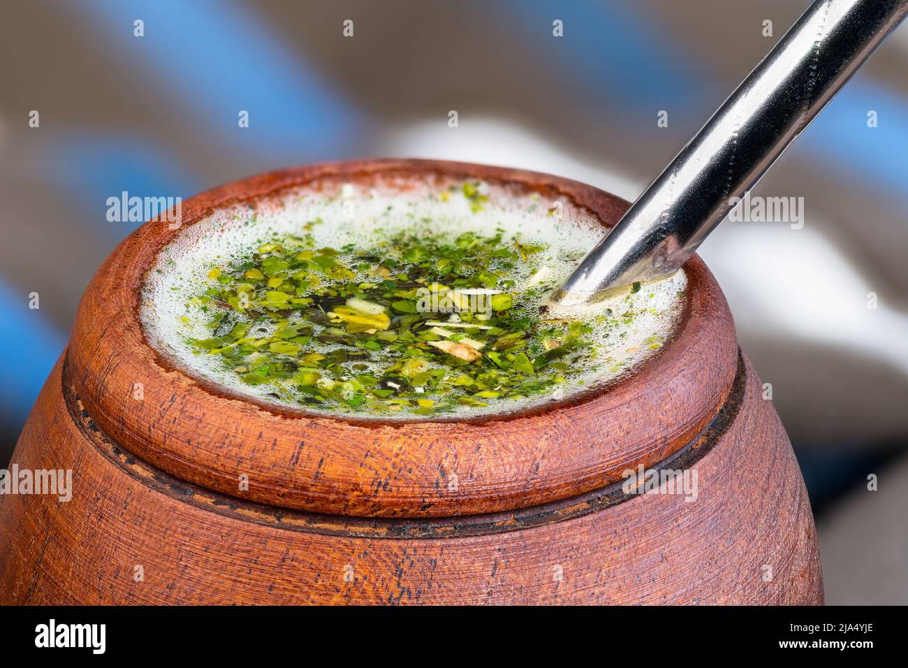 Wood cup of hot yerba mate with metal bombilla straw detail. Dried green holly leaves and white froth in herbal tea. Traditional South American drink. Stock Photo