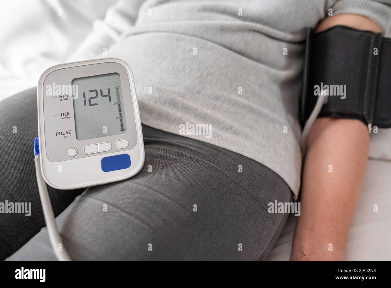 A woman is testing her blood pressure while lying in bed. Stock Photo