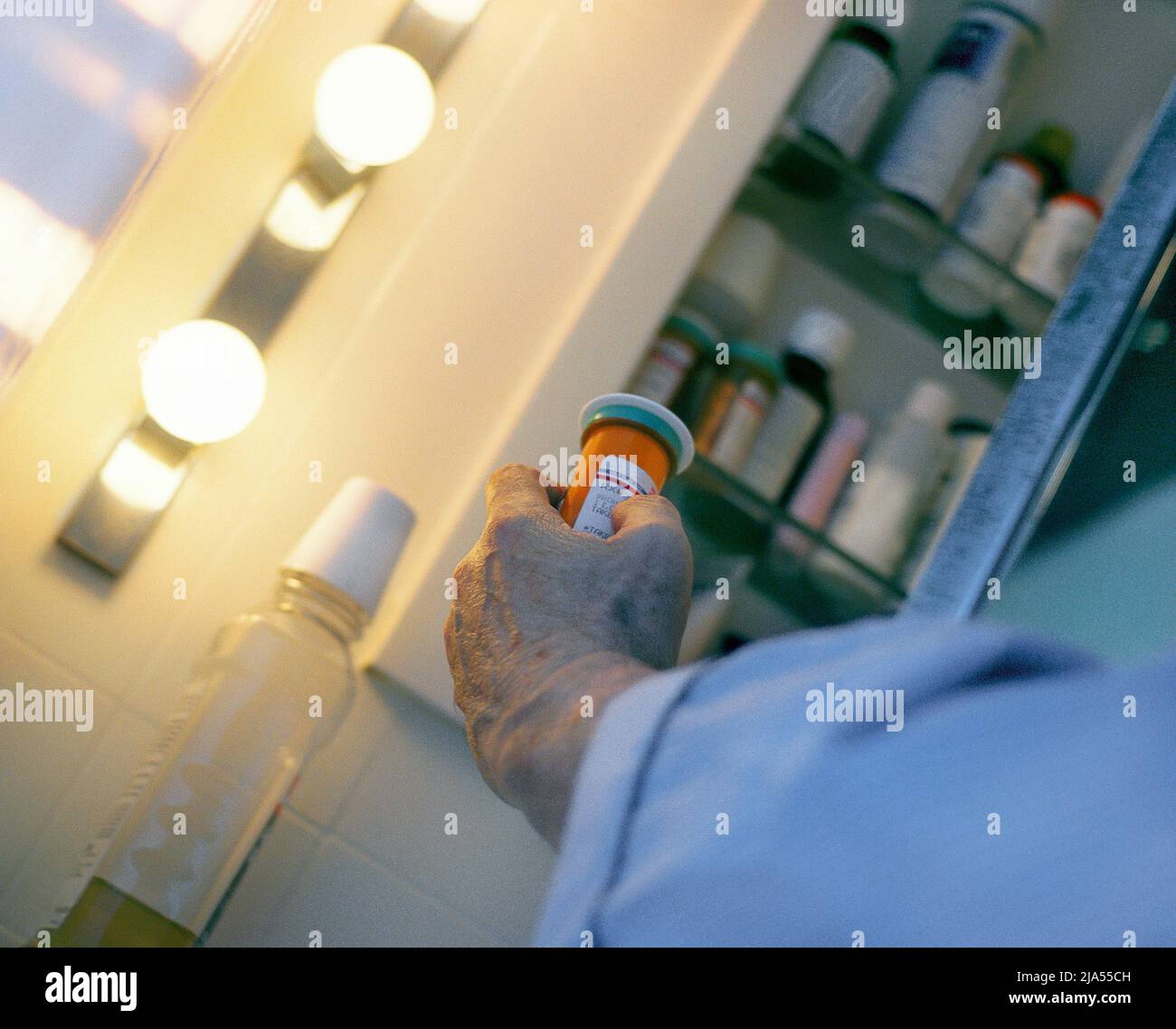 Man taking medication from open medicine cabinet in the bathroom. Senior reading label on pill bottle before medicating. Cautious. Stock Photo