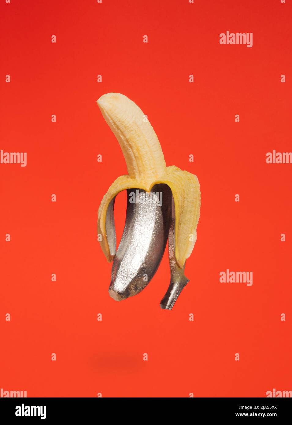 Painted silver peeled banana on orange background. Minimal retro futurism background. Creative summer fruit concept. Stock Photo