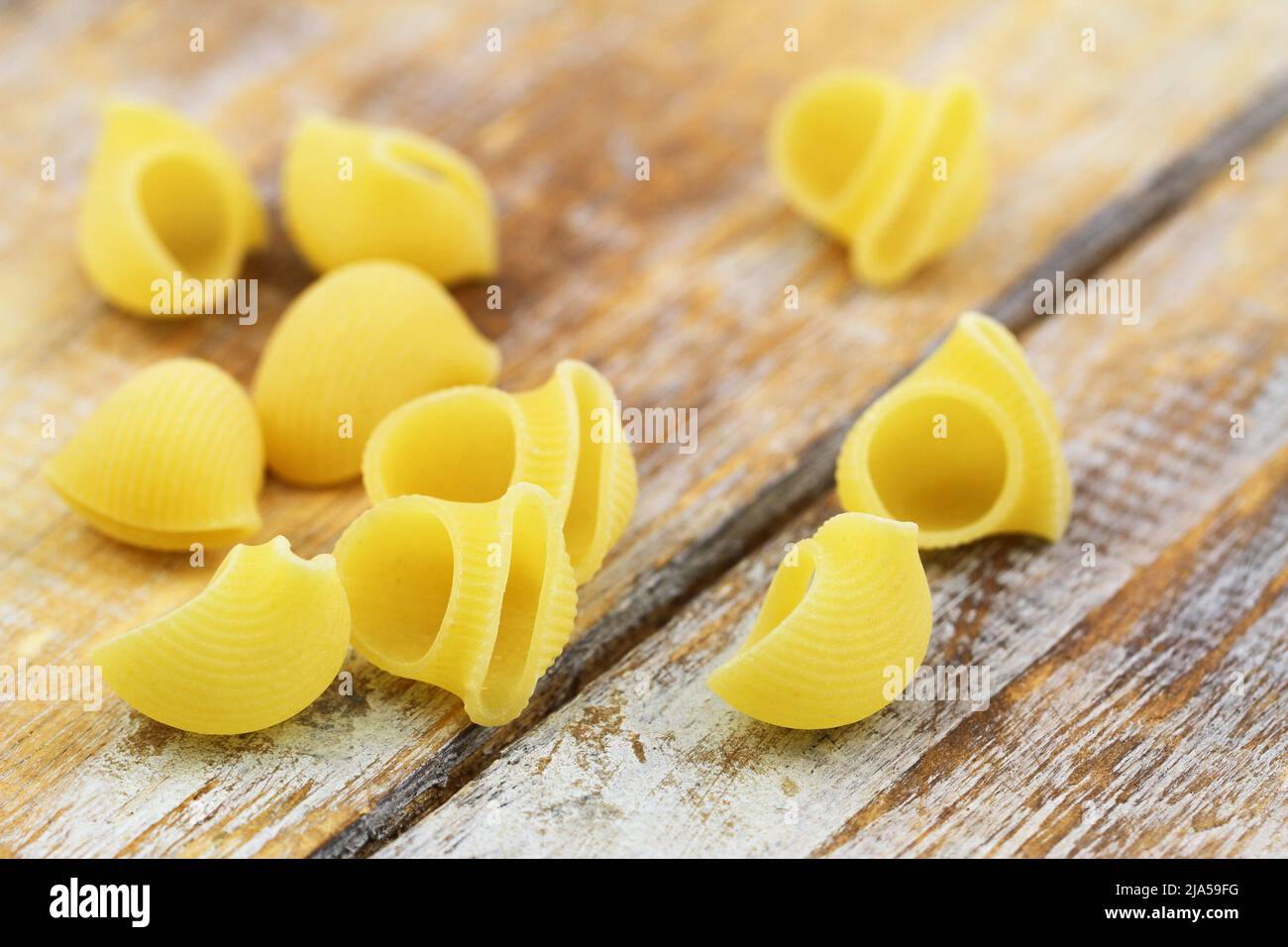 Uncooked Italian pasta scattered on rustic wooden surface Stock Photo