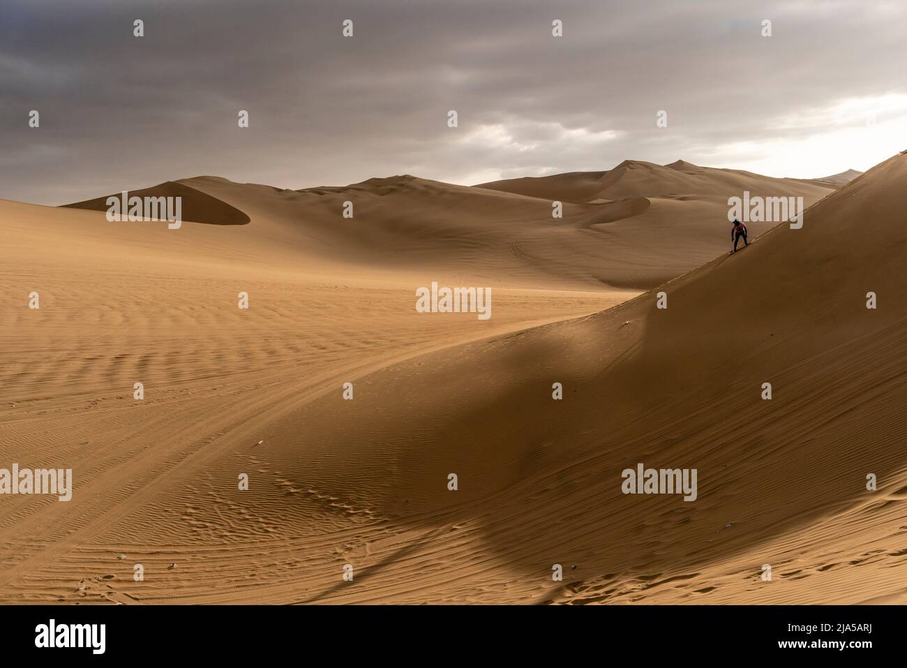 A Man Sandboarding On The Sand Dunes Of Huacachina, Ica Province, Peru. Stock Photo