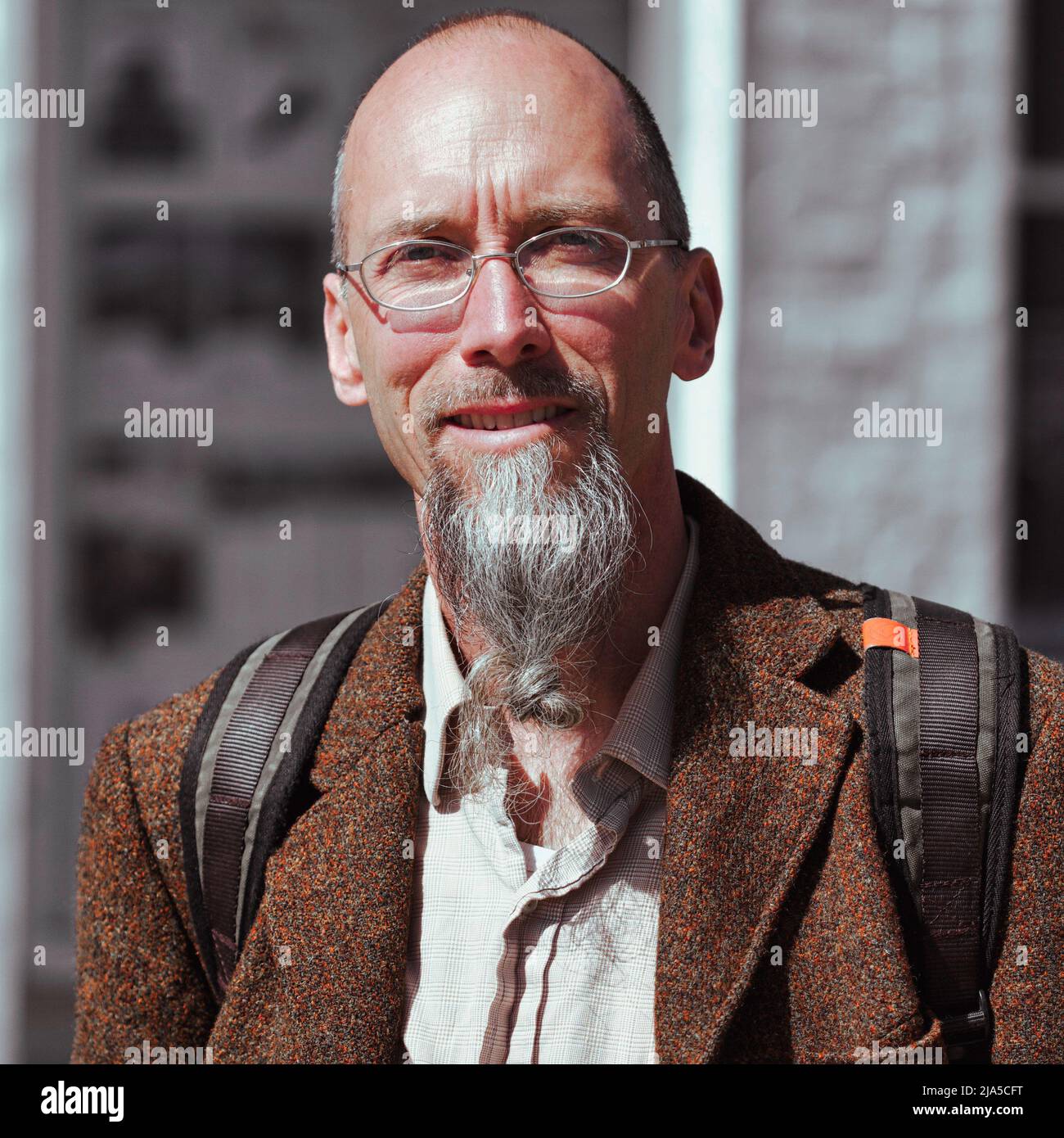 Man with a grey goatee beard in an orange tweed jacket stops for a street portrait in the sun in Truro, Cornwall. Stock Photo