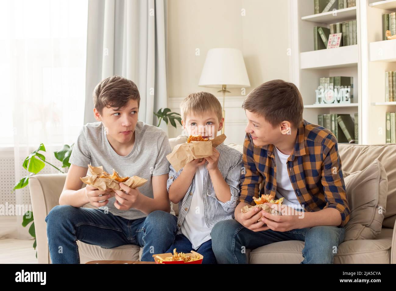 A cute three teenage boys, eating fast food in living room Stock Photo