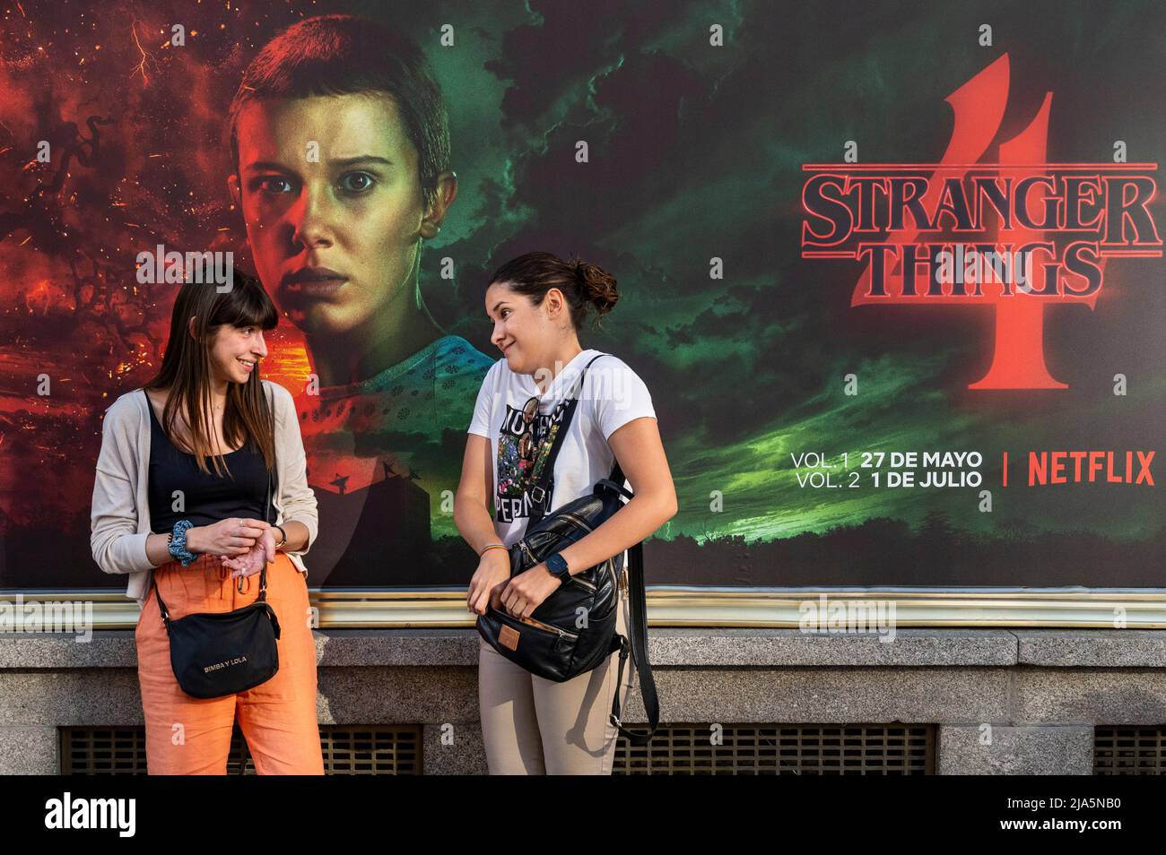 Madrid, Spain. 28th May, 2022. Women talk in front of a street commercial advertisement banner from the American global on-demand Internet streaming media provider Netflix featuring Stranger Things Season 4 TV show in Spain. Credit: SOPA Images Limited/Alamy Live News Stock Photo