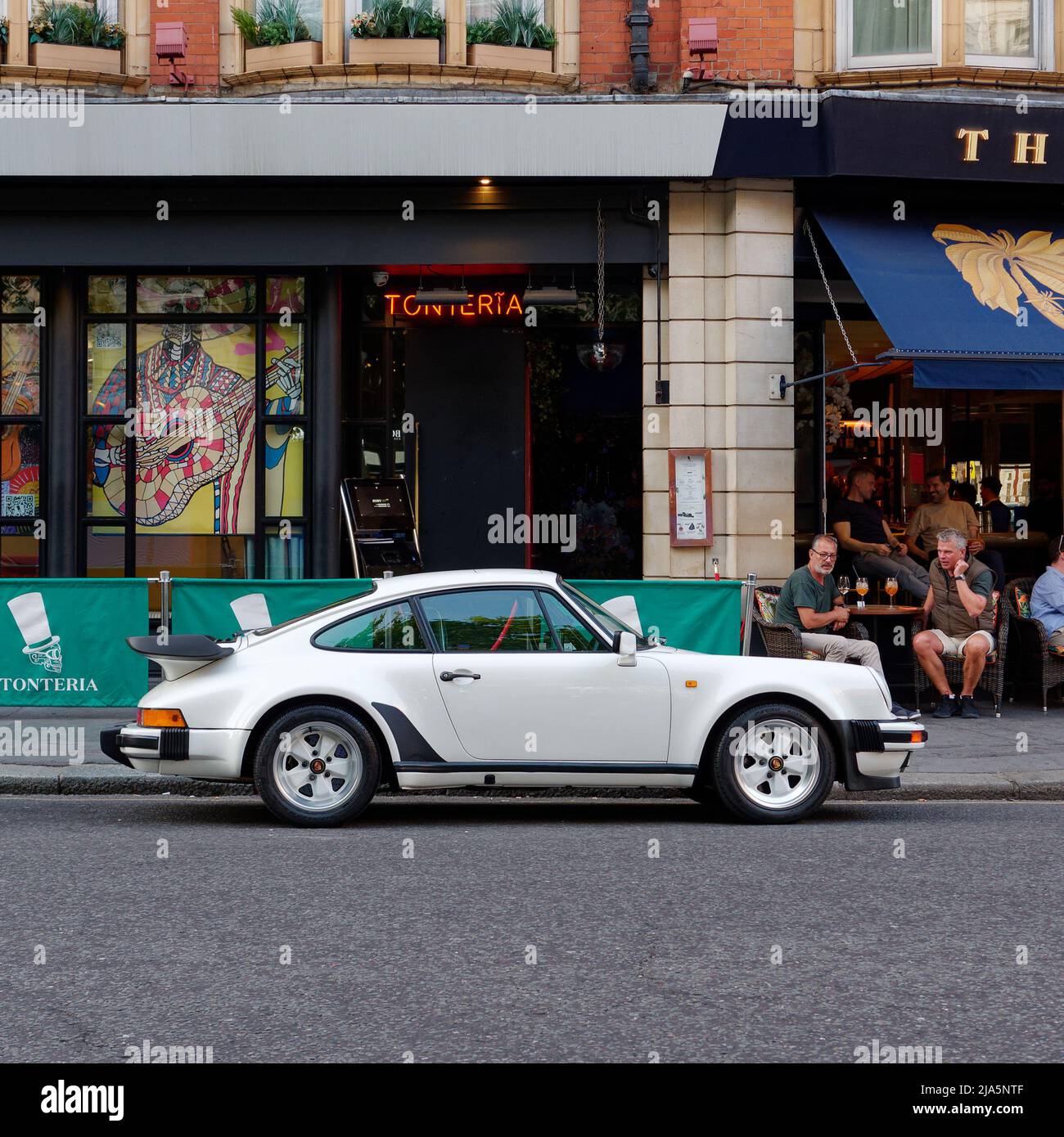 London, Greater London, England, May 14 2022: White Porsche 911 Carrera parked in Sloane Square Chelsea as people sit at a nearby bar or restaurant. Stock Photo