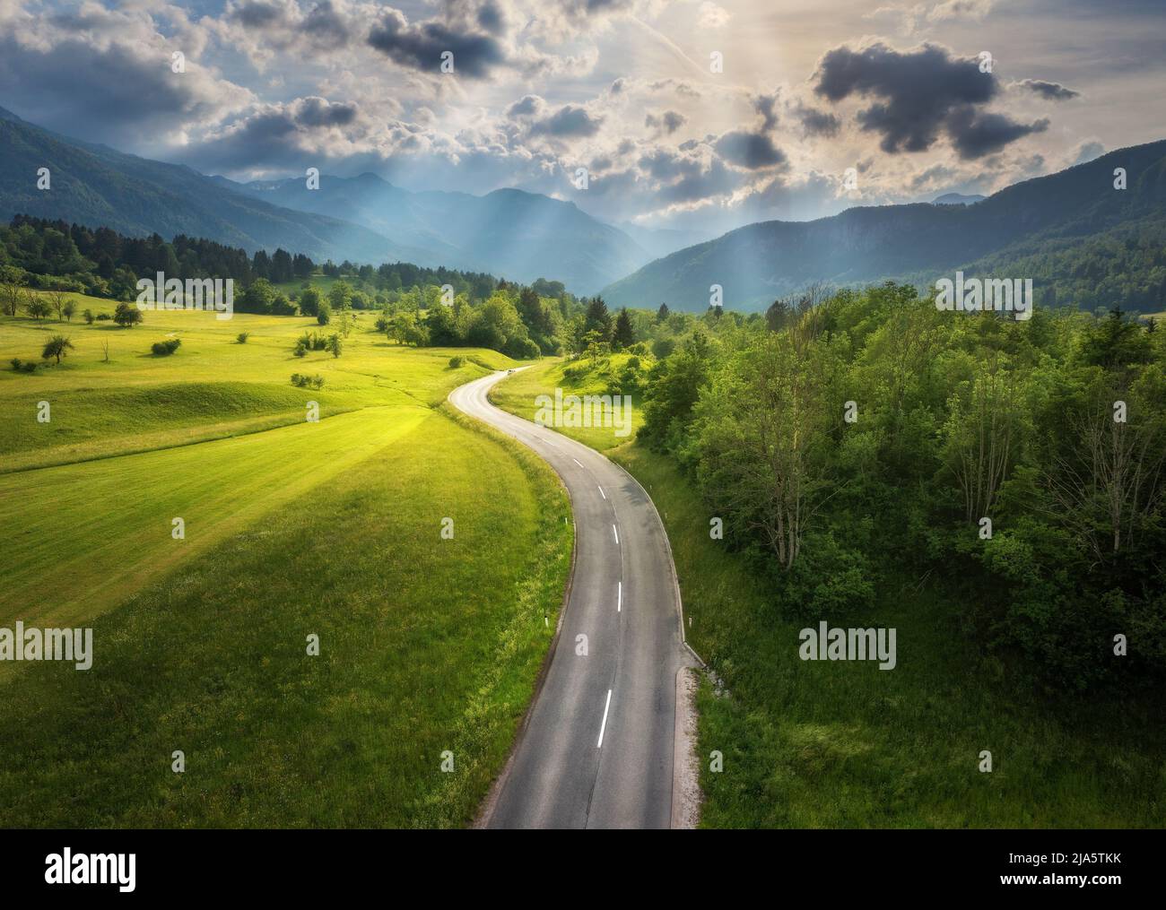 Aerial view of road in green meadows and hils at sunset in summer Stock