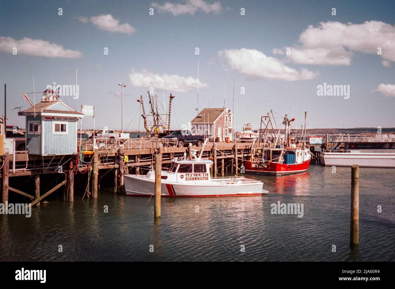 The Plymouth harbor master secures his white and red boat to the dock on a bright evening at Plymouth Massachusetts. The image was captured on analog Stock Photo