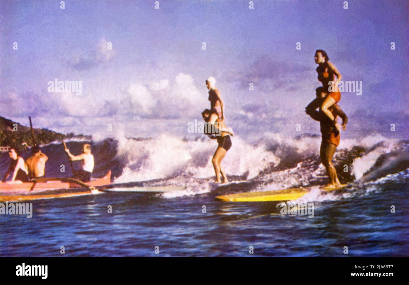Vintage color postcard image of tandem surfing and outrigger canoeing at Waikiki Beach in Honolulu, Hawaii, c1950s. Stock Photo