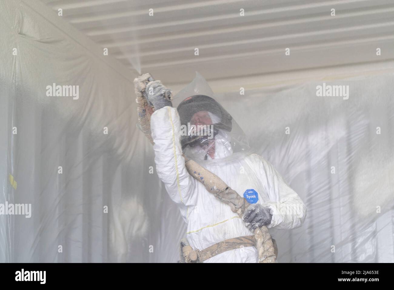 A workman sprays a shipping container ceiling with Grapho Therm to prevent the build up of condensation. Stock Photo