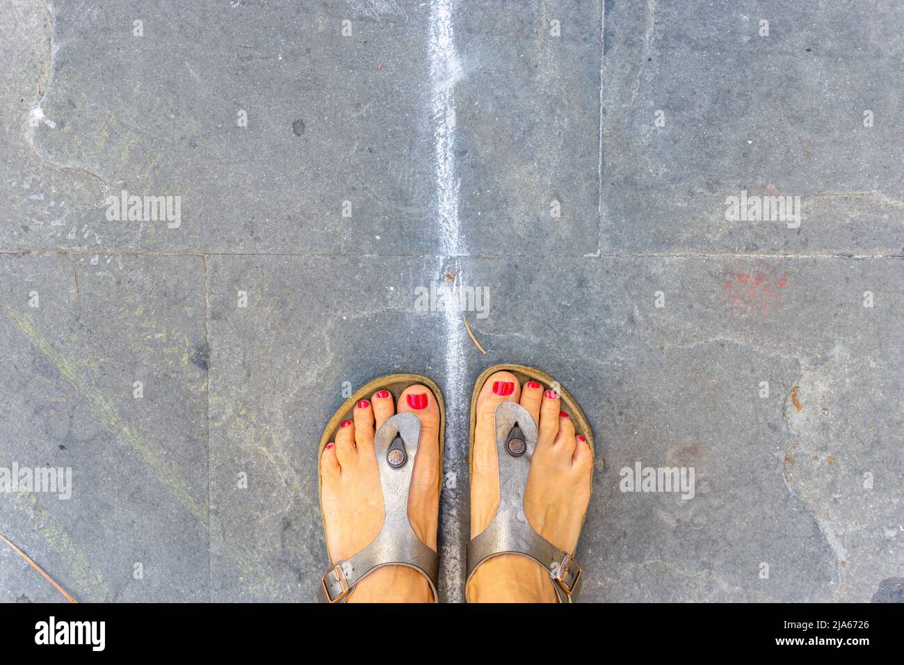 Grado, Italy - July 8, 2021: Feet in open sandals with red nail polish on toes Stock Photo