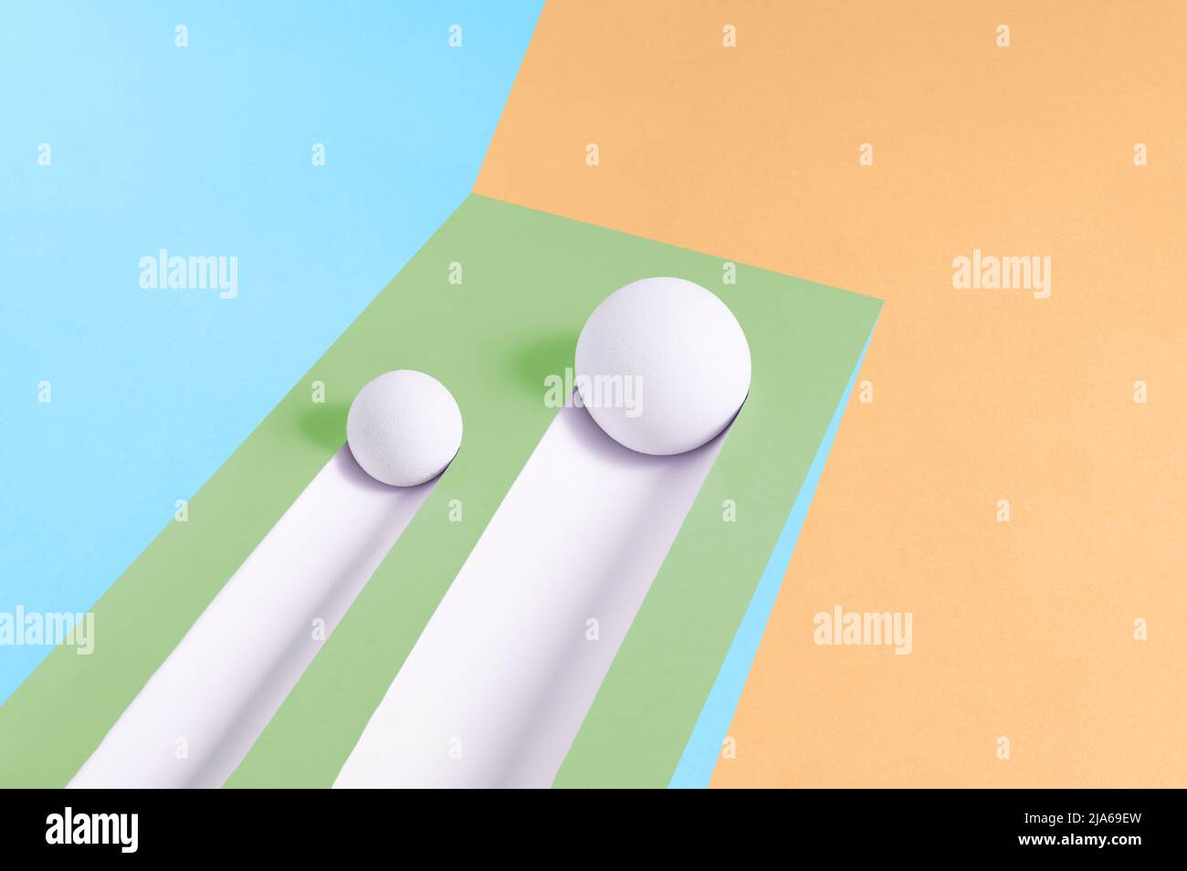 Two white balls roll downhill and leave a trail on a multicolor background. Abstract minimal concept. Isometric rectangle with copy space. Geometric s Stock Photo