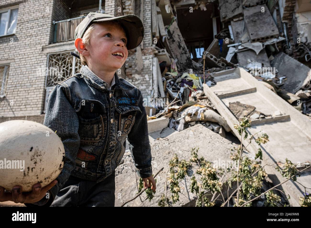 Bakhmut, Ukraine. 24th May, 2022. A child is playing in front of the ruins of the residential building destroyed by Russian artillery strikes in Bakhmut, Donbas. As Bakhmut stands as a key city to Ukrainian forces in defending Donetsk(Donbas) region, the city is under attack by the Russian troops. The Russian invasion of Ukraine started on February 24, the war that has killed numerous civilians and soldiers. Credit: SOPA Images Limited/Alamy Live News Stock Photo