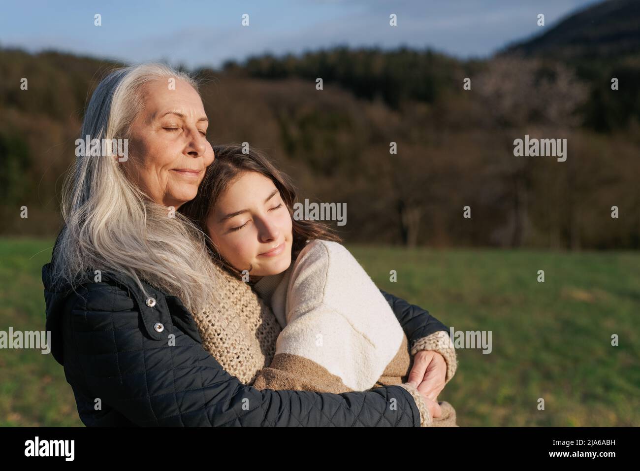 Happy senior grandmother with teenage granddaguhter hugging in nature on spring day. Stock Photo