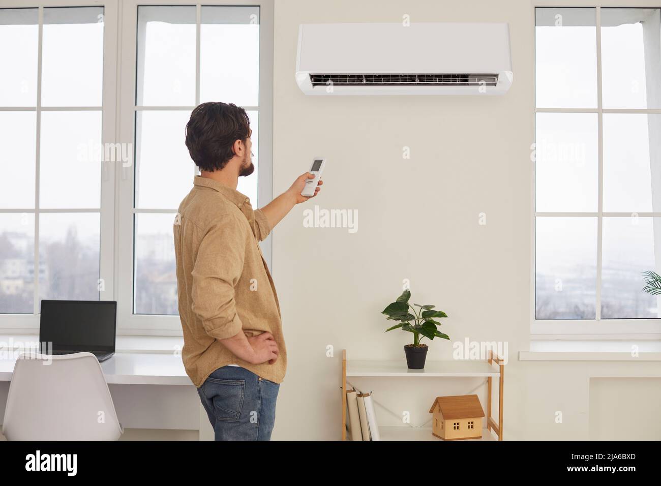 Man with remote control from air conditioner creates comfortable temperature for himself. Stock Photo