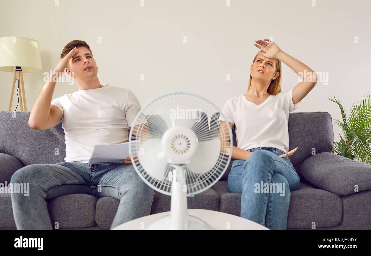 Exhausted woman and man sitting in front of electric fan sweating