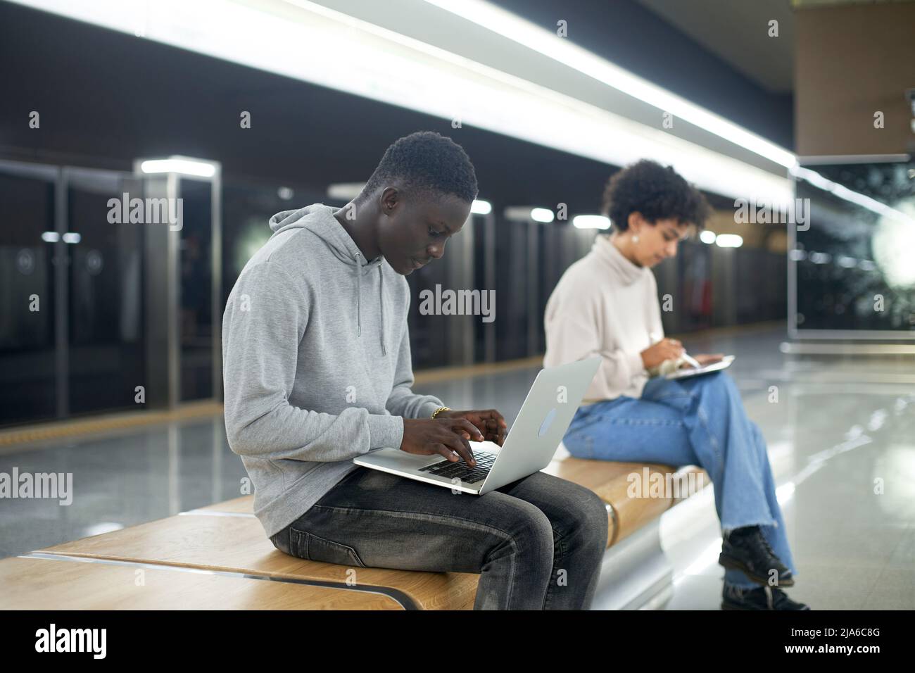 young people using their devices while sitting on a bench in the Stock Photo