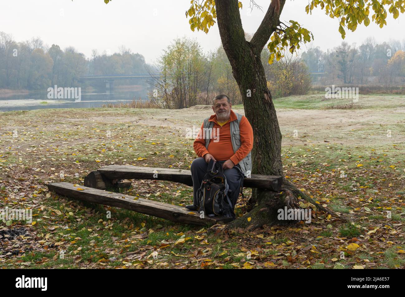 lonely senior tourist having short rest under tree at autumnal seas in inSumskaya oblast, Ukraine Stock Photo