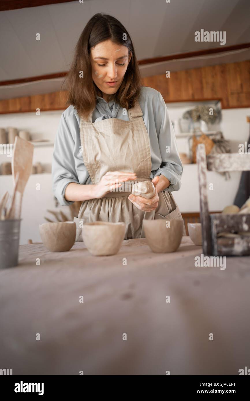 female artisan concentrated on modeling jug from raw clay while pottery lesson or workshop in creative studio. Woman ceramic business owner making Stock Photo