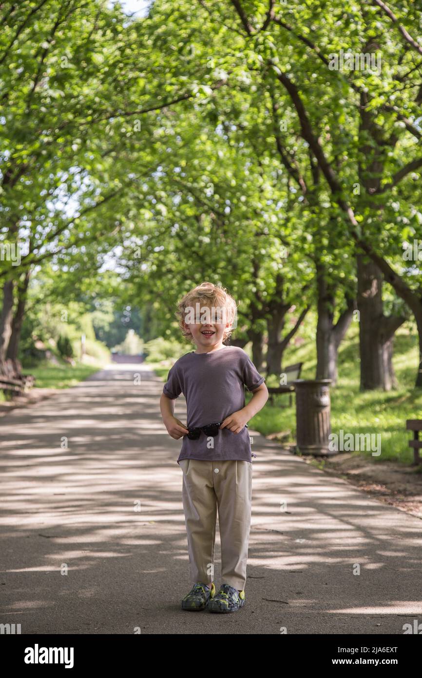 boy standing in the park.a curly-haired boy of five years stands smiling in a green park Stock Photo