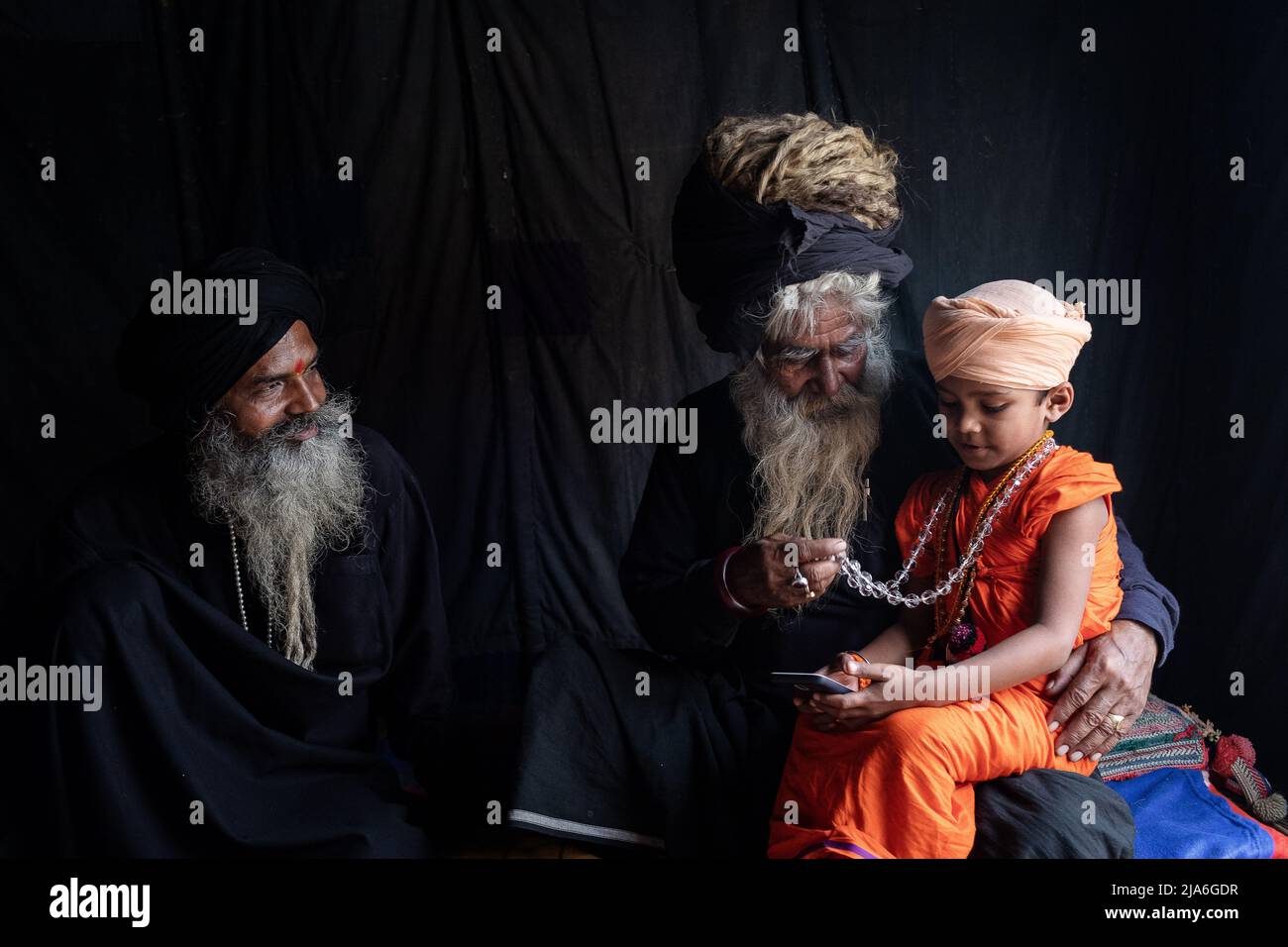 Two holy men take care of a child sadhu in their tent at the Kumbh Mela festival. Every twelve years, millions of Hindu devotees begin a massive pilgrimage to the most sacred of Indian festivals: the Kumbha Mela, which takes place in Prayagraj, a place considered particularly auspicious because it is at the confluence of the Ganges, Yamuna and the mythical Saraswati. It is estimated that in 2019, 120 million people attended the sacred enclosure over the course of a month and a half. These numbers, equivalent to the total population of Japan, and 40 times the number of pilgrims who visit Mecca Stock Photo