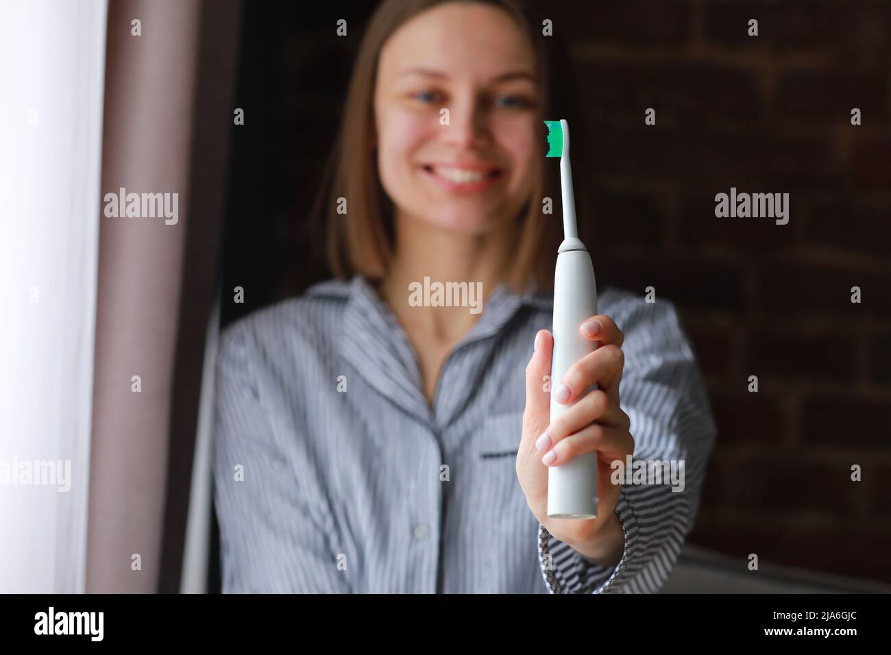 Happy healthy smiling woman with ultrasonic electric brush in bathroom