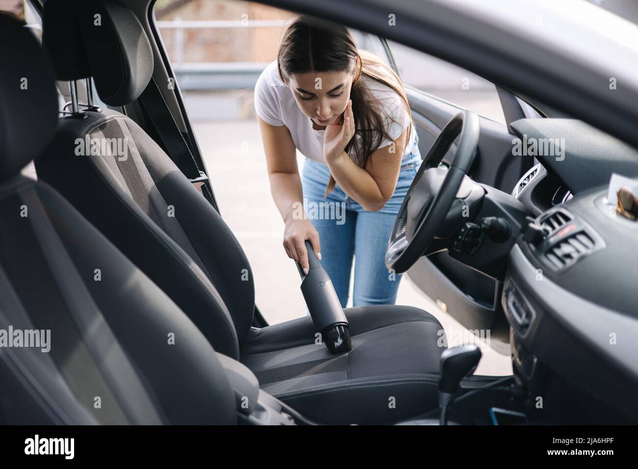 Woman vacuuming her car in the garage at home. Female using portable