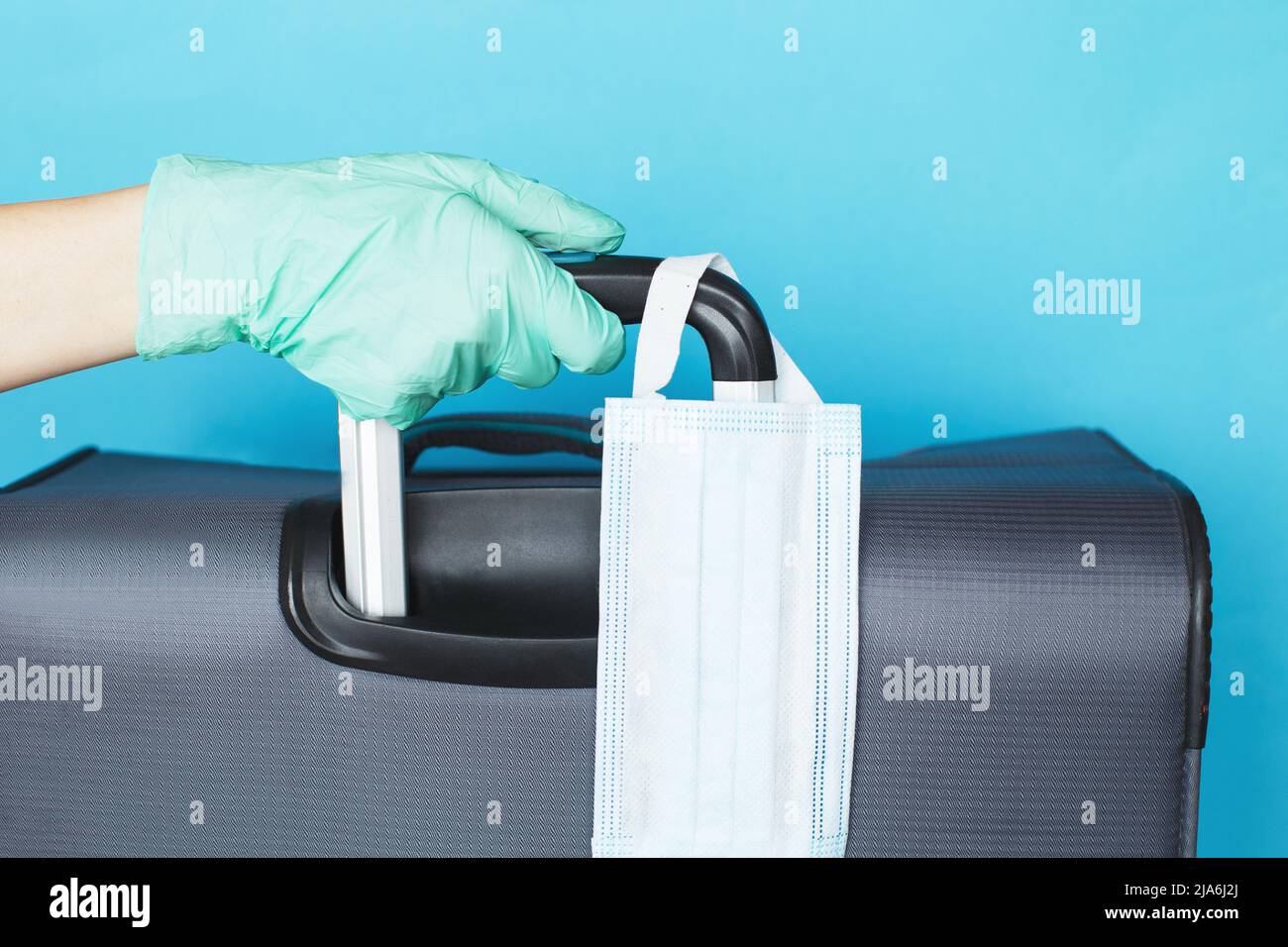 Hand with a luggage bag and medical mask isolated on a blue background. protection Coronavirus disease Covid-19 infection. Stock Photo