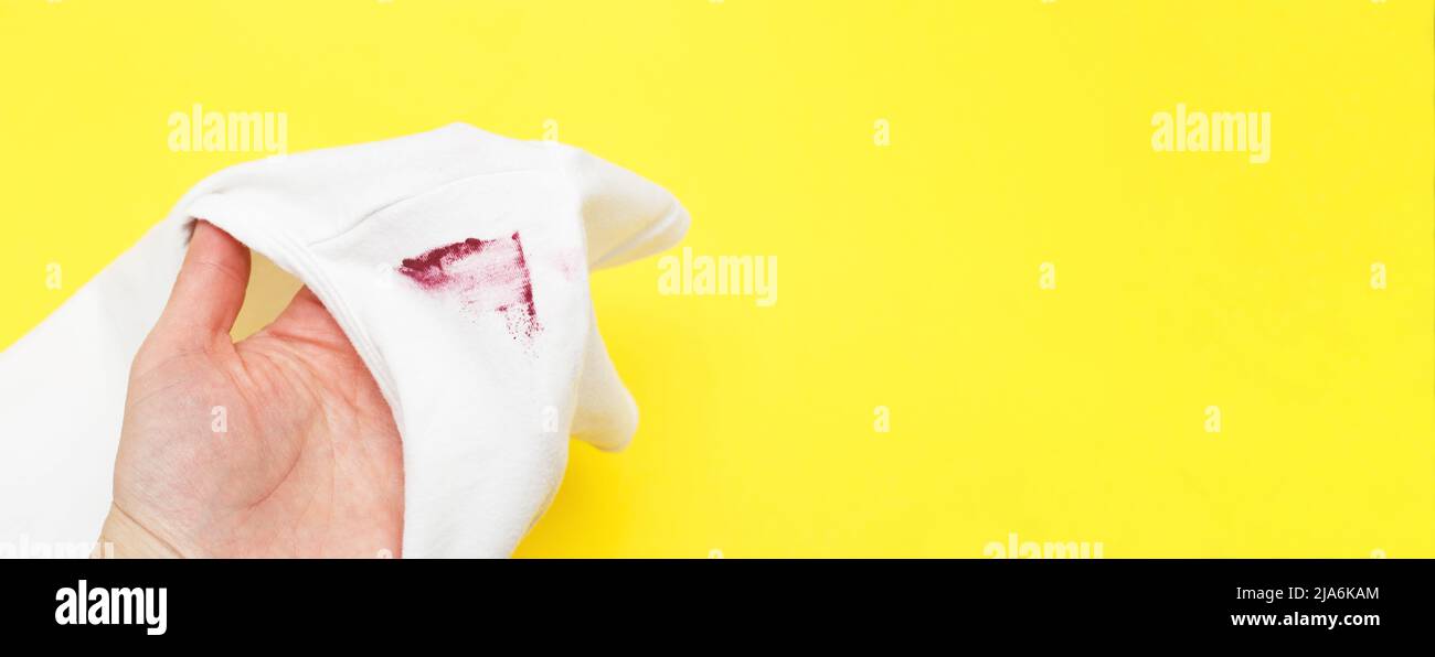 female hand holding white shirt with red lipstick stain on yellow background. banner Stock Photo